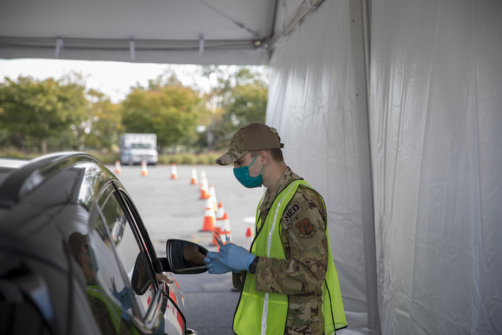 A member of the Delaware National guard talks with a member of the public during a drive-thru COVID-19 vaccine clinic.” style=