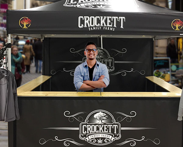 man standing behind counter of custom-printed, black, crocket farms pop up tent