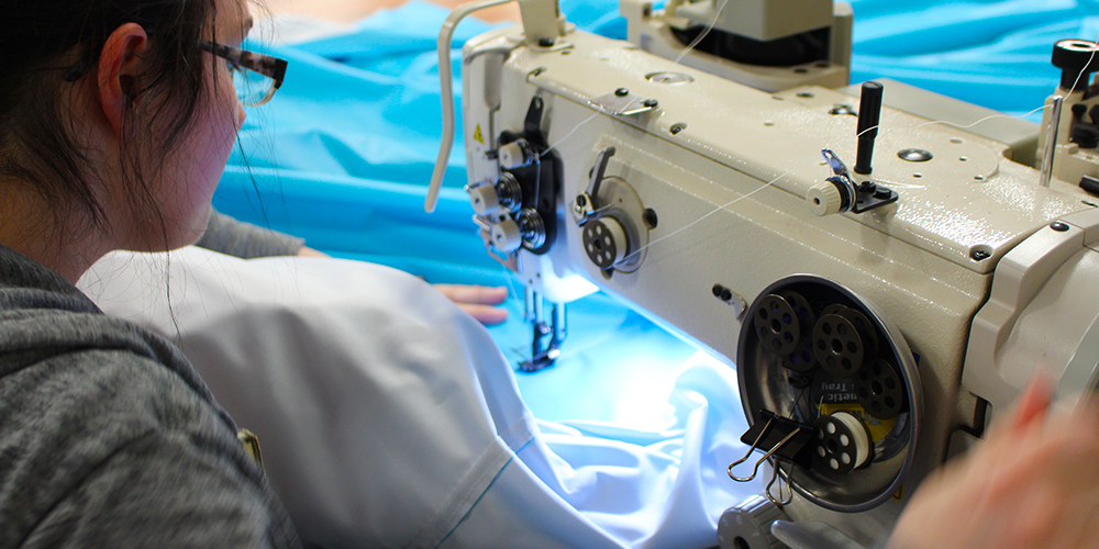 A blue tent canopy working through a skilled fabricators sewing machine.