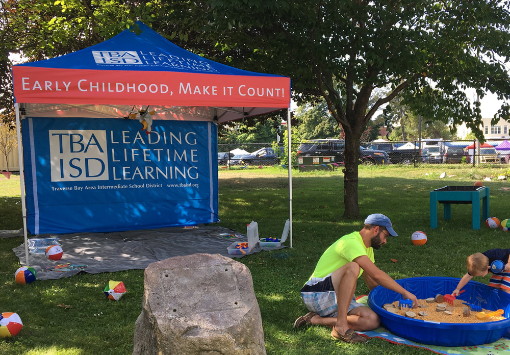 Children playing in sandbox in-front of pop-up tent printed with Early Childhood branding.
