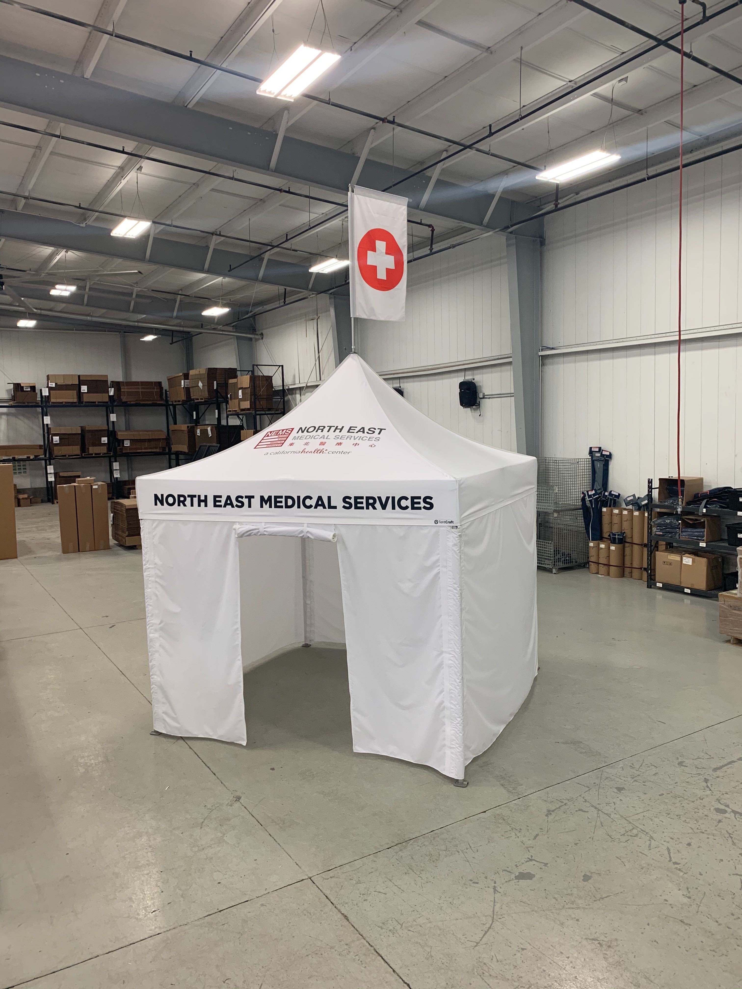 White 10x10 medical tent with custom peak flag, printing, and a roll up entrance on the TentCraft production floor