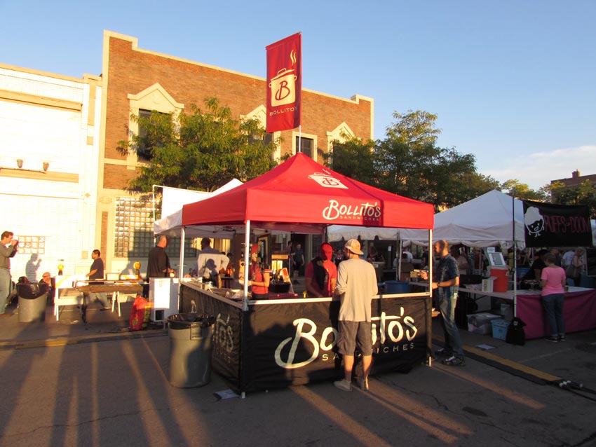 A 10x10 mobile food vendor heavy-duty pop-up tent with red peak flag used for product sampling.